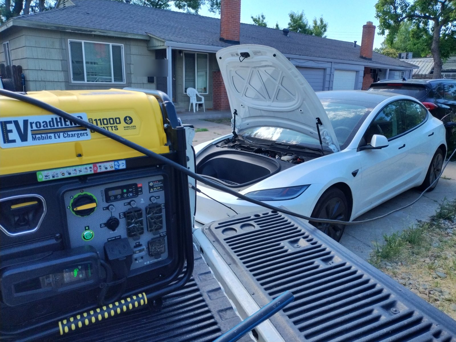 White Tesla Model 3 charging in a residential driveway from a truck-mounted mobile EV charger